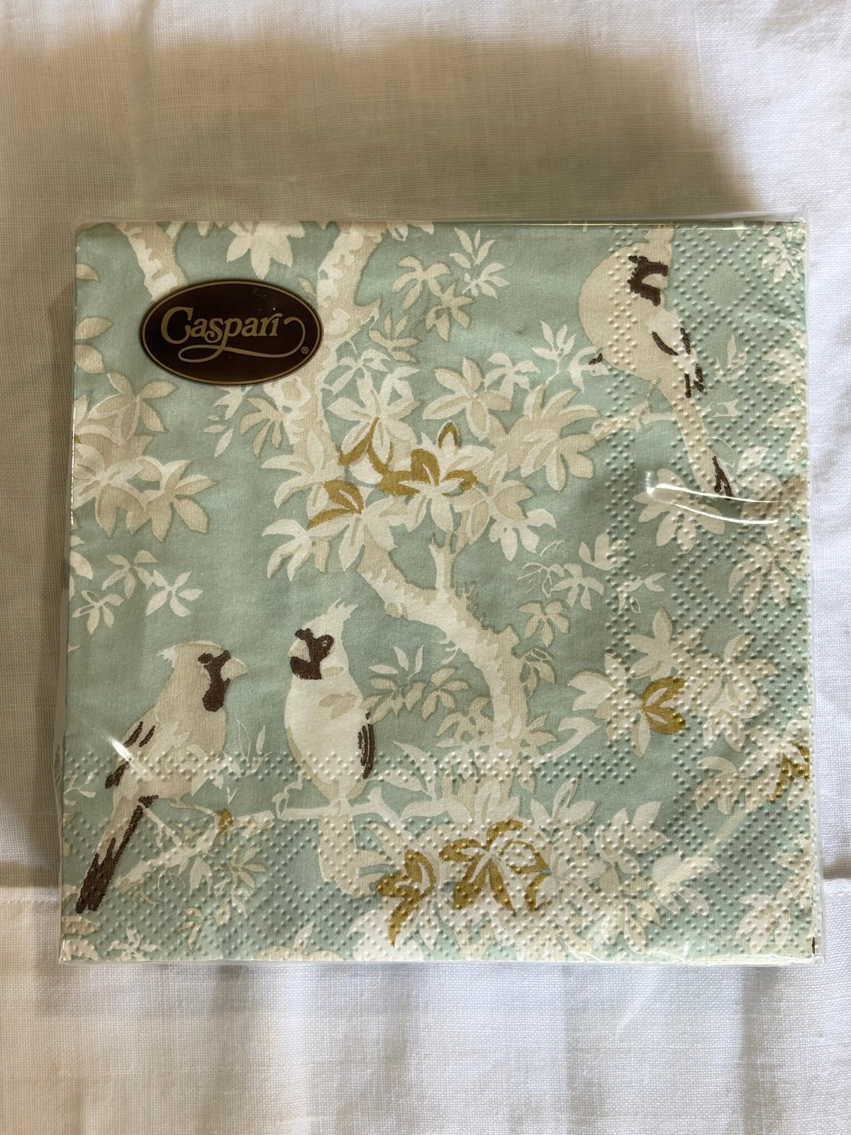 Paquete de servilletas de aves y follaje sobre fondo celeste, visto de frente