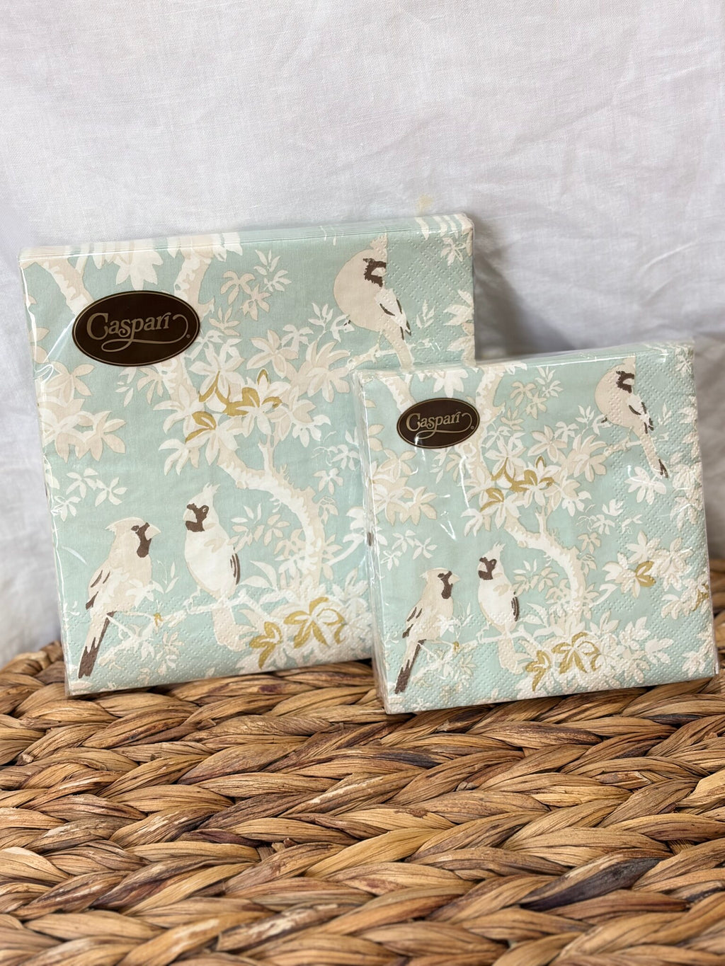 Servilletas de papel con aves entre ramas sobre fondo celeste, los dos formatos sobre fibra natural