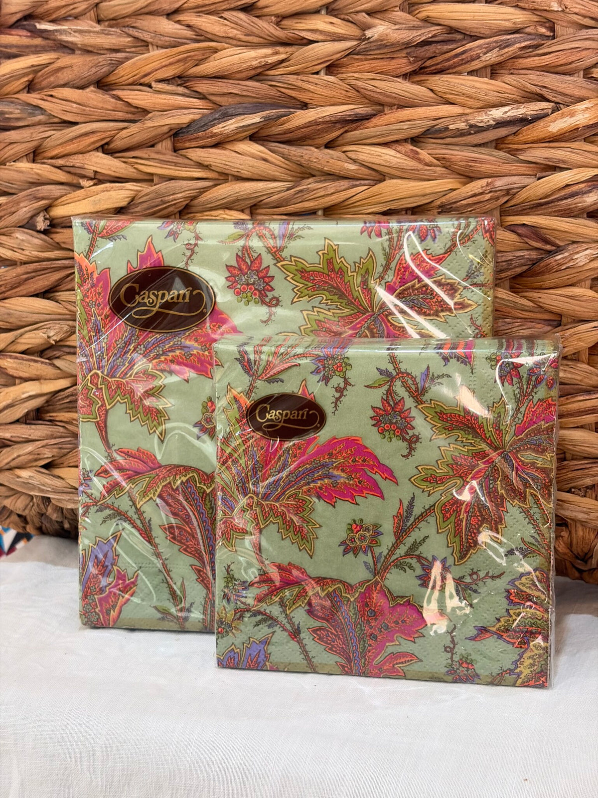 Dos paquetes de servilletas de estampado floral sobre fondo verde, apoyados en fibra natural