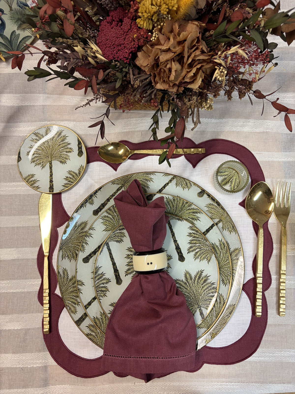 Mesa puesta con servilleta granate, mantel individual granate y plato de palmeras