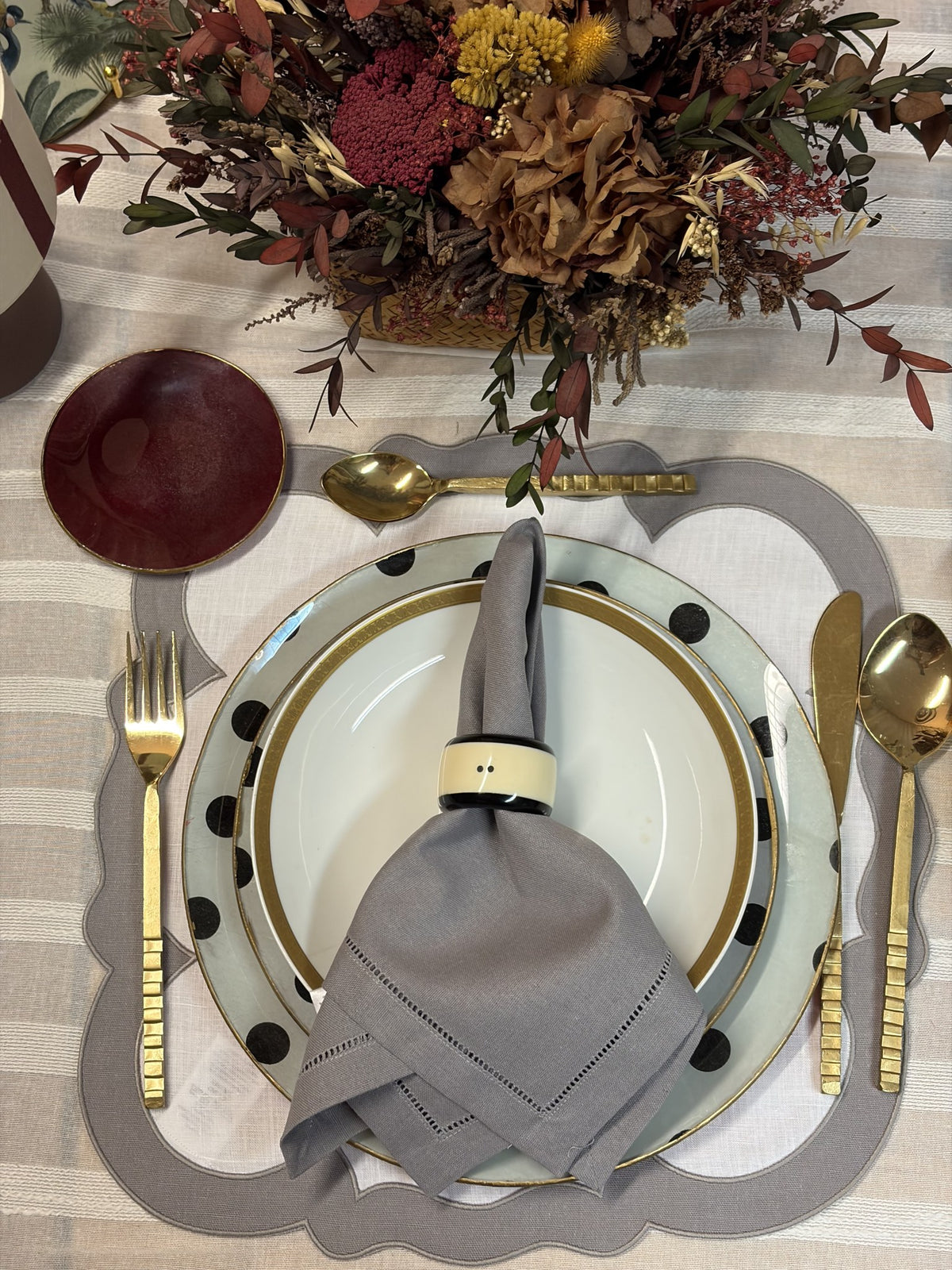 Mesa puesta con servilleta gris, mantel individual gris y vajilla de lunares