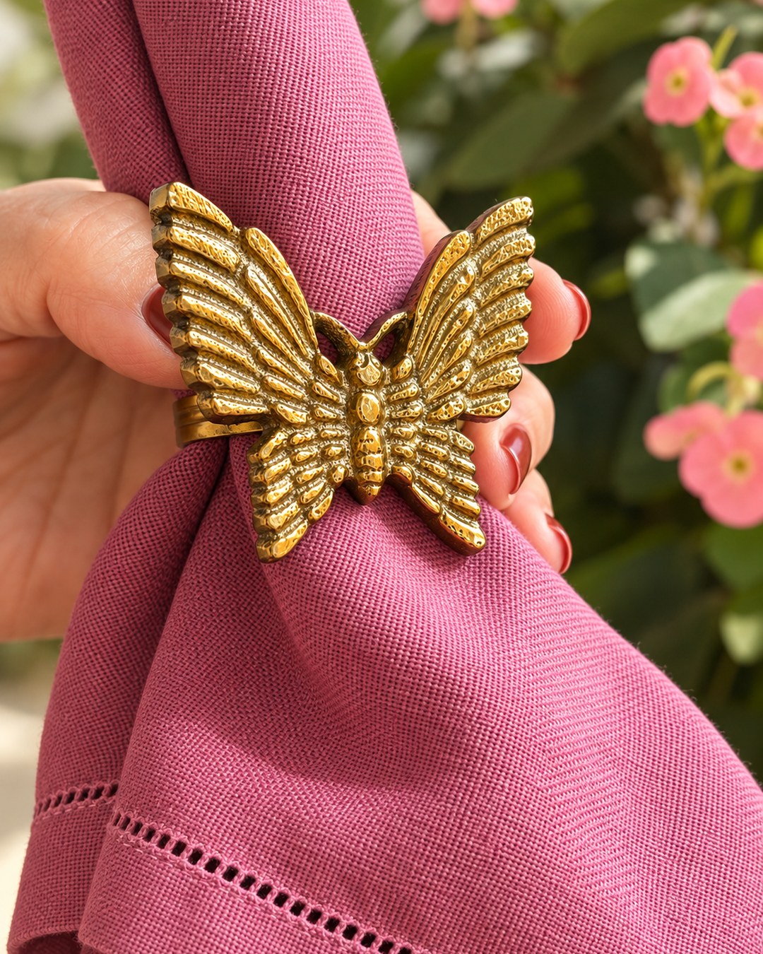 Servilletero Mariposa dorado sujetando una servilleta de lino rosa